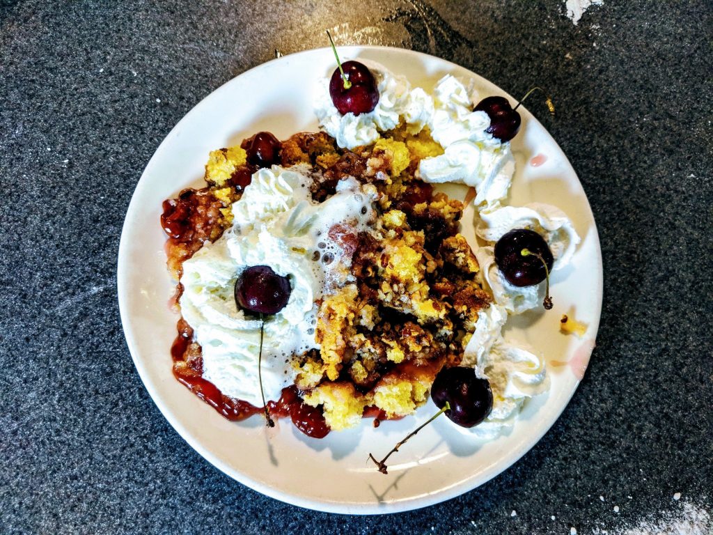 Cherry cobbler, garnished with fresh cherries and whipped cream on top