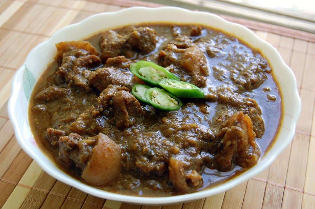 A dark brown curry broth with a hearty amount of pork, garnished with jalapeno