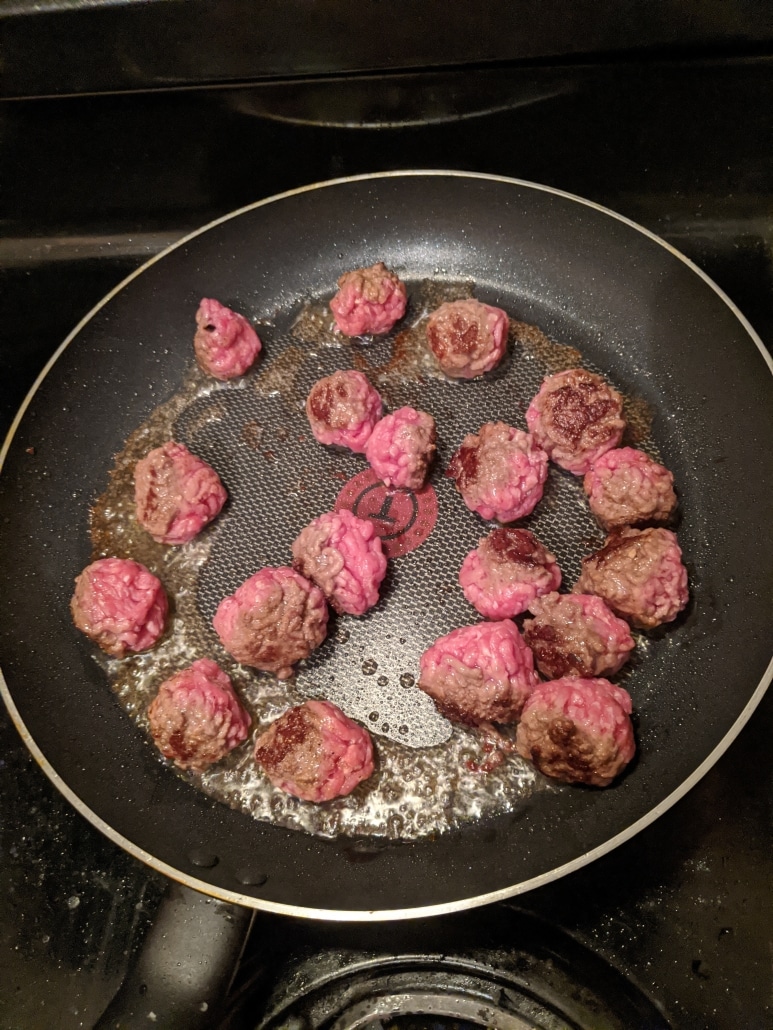 Browning meatballs before adding them to the pot.
