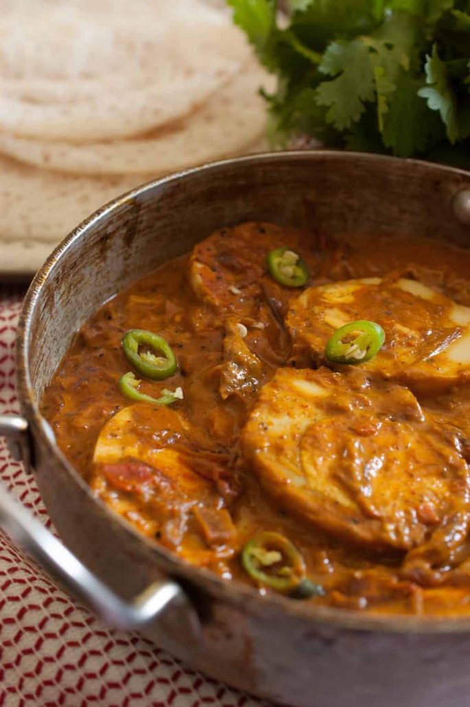 A brown curry gravy with large halves of egg, jalapenos, tomatoes, and onion