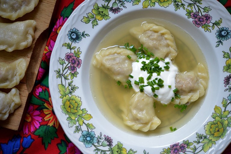 Unleavened dough dumplings in a clear chicken soup with sour cream and chives on top