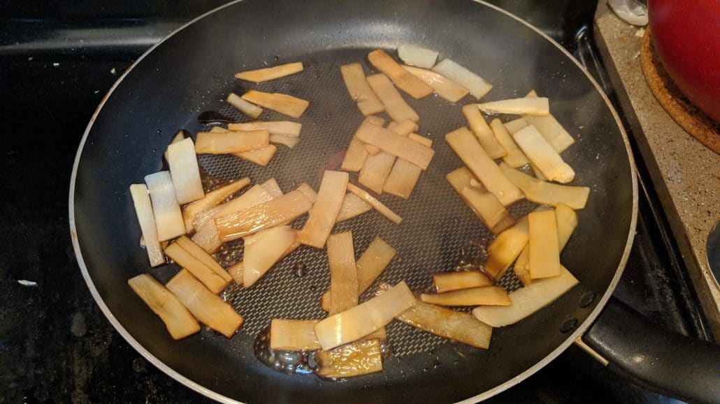Bamboo shoots being cooked with soy sauce and miso paste in a skillet