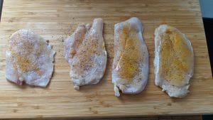 Seasoned chicken cutlets on a cutting board